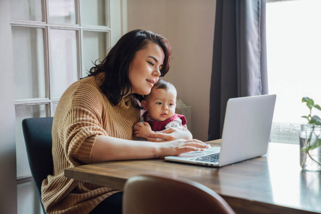 Mother holding a baby while looking at a laptop for title services from Quaint Oak Abstract